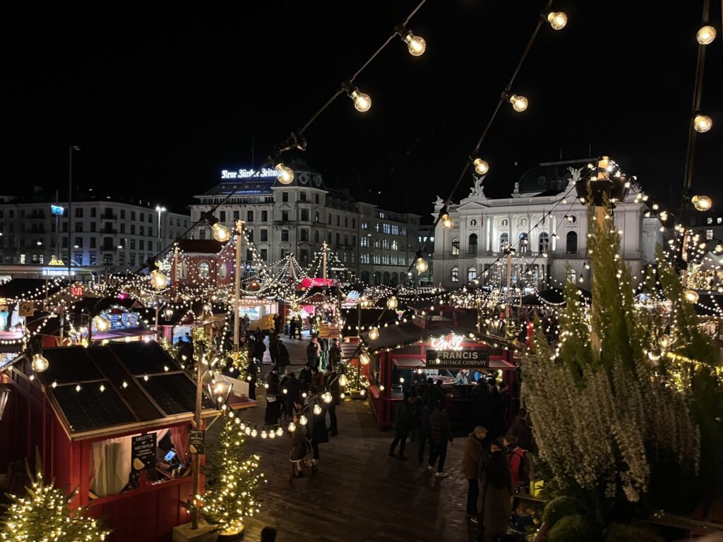 View of Wienachtsdorf Christmas market at night with wooden chalets and stalls decorated with Christmas lights.