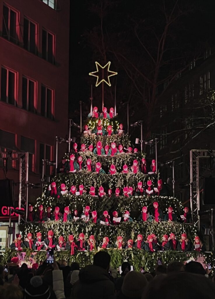 Choir members dressed in red robes arranged in Christmas tree formation performing at Werdmühleplatz Christmas market in Zurich