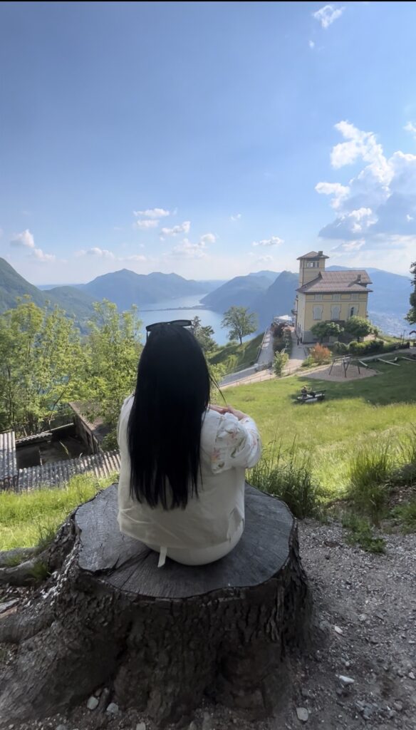 Travel blogger Eleni Kotidou (worldtravellen.com) with the Vetta cafe-restaurant in view at Monte Bre, Lugano, Switzerland